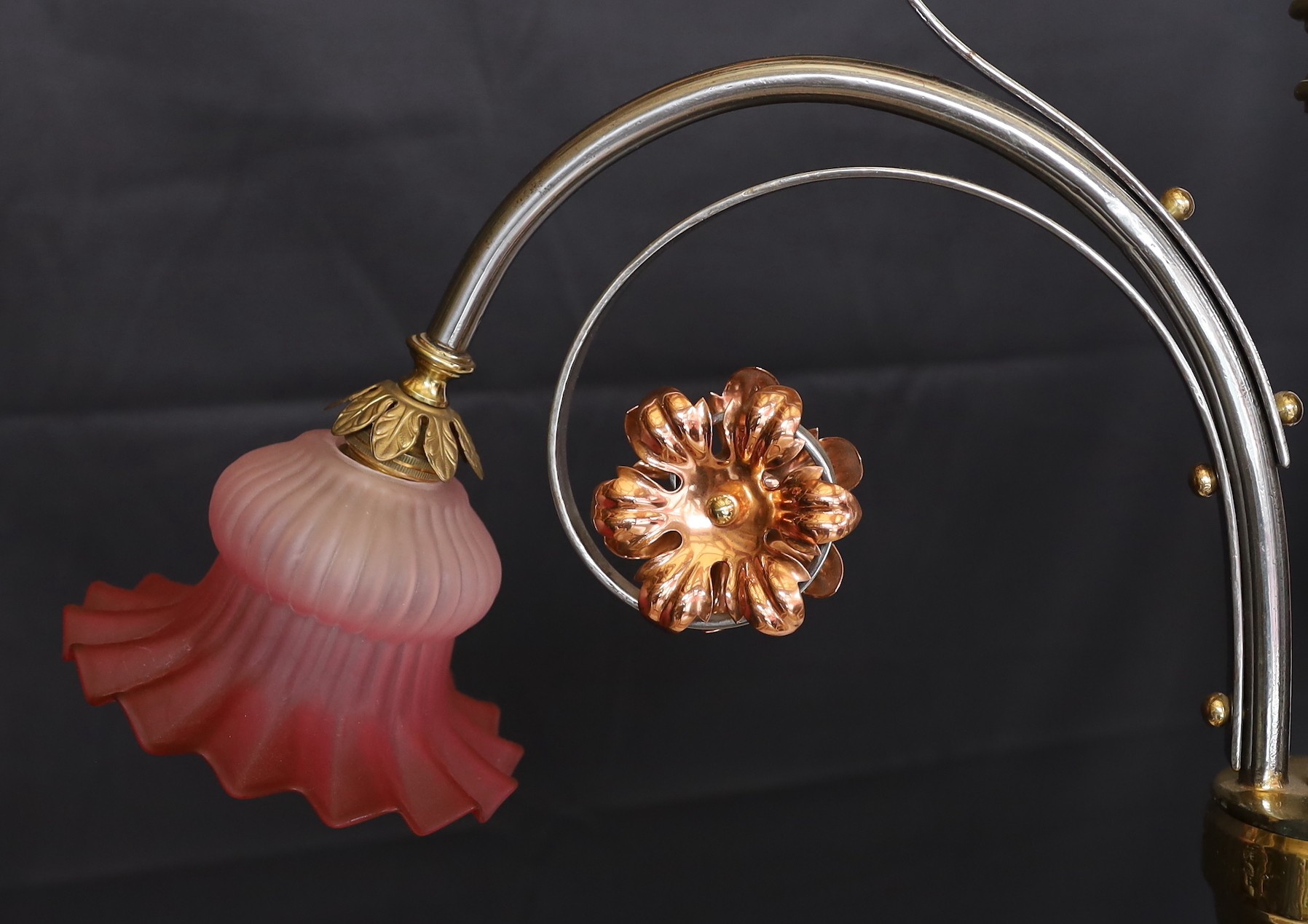 An English Arts & Crafts wrought iron brass and copper three light electrolier with pink tinted opaque glass shades, height 60cm. width 66cm